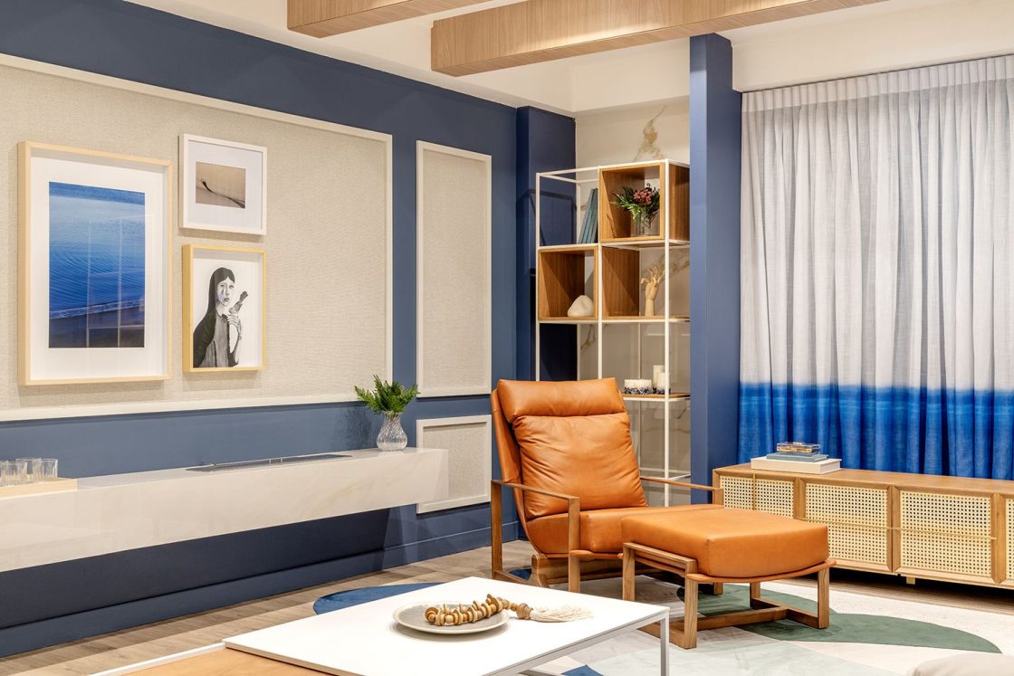 Living com piso amadeirado, poltrona em couro marrom, fundo neutro e claro e detalhes azuis