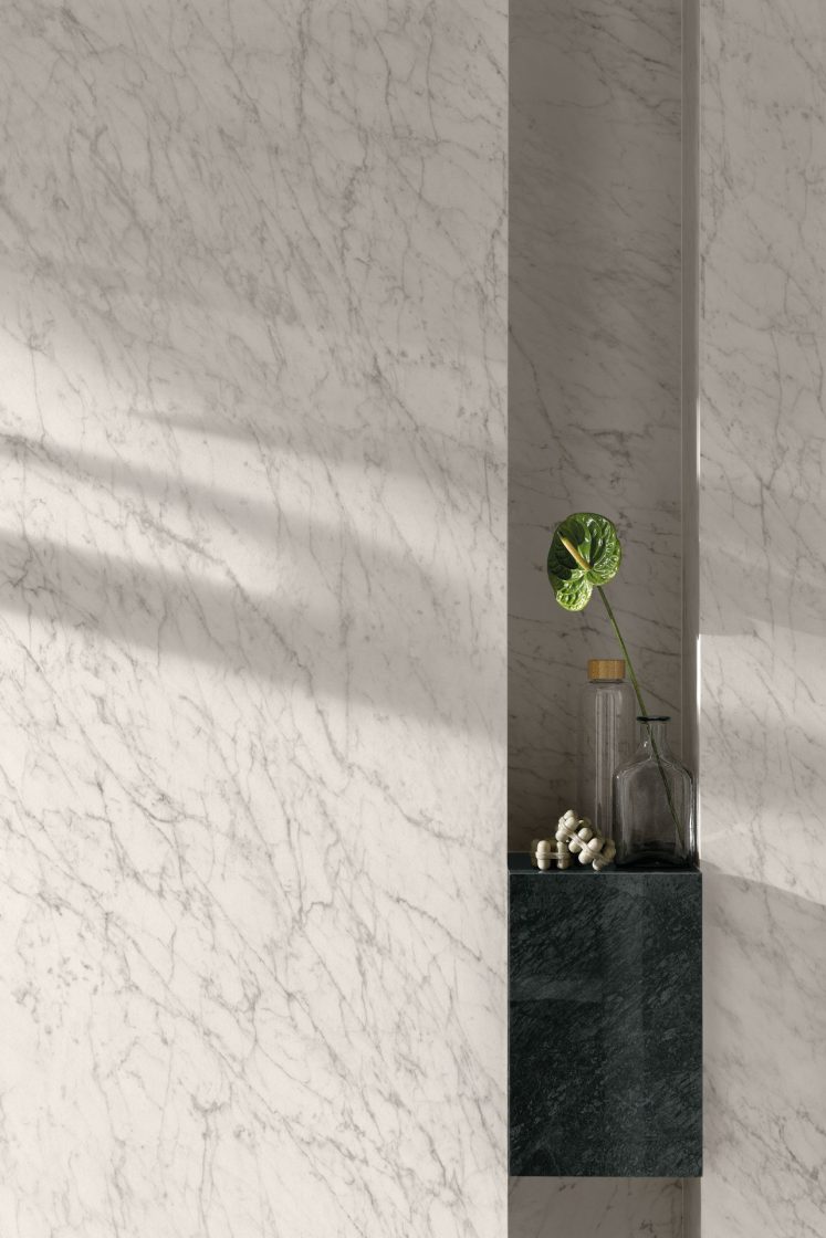 Detalhe de parede de ambiente com revestimento que reproduz mármore branco e bancada em mármore verde-escuro ao fundo