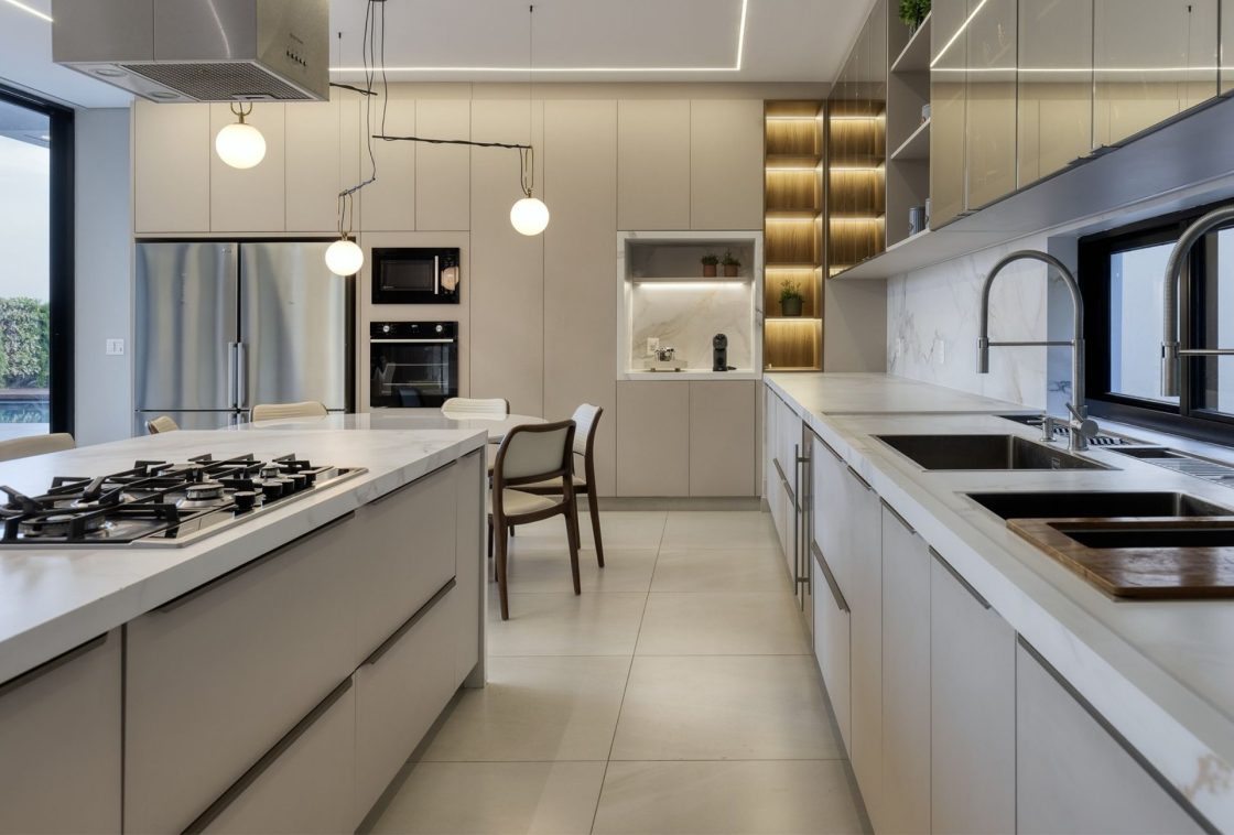 Torre quente com micro-ondas e forno embutidos em marcenaria off-white, integrada a cozinha ampla com ilha central em mármore e cooktop a gás