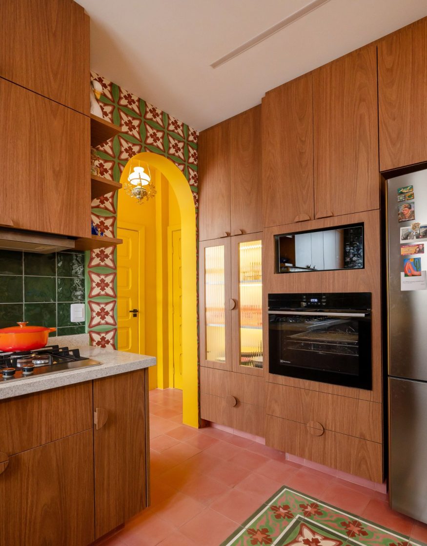 Torre quente com forno embutido em marcenaria de madeira, integrada a cozinha com ladrilhos hidráulicos coloridos, arco amarelo e revestimento verde na bancada