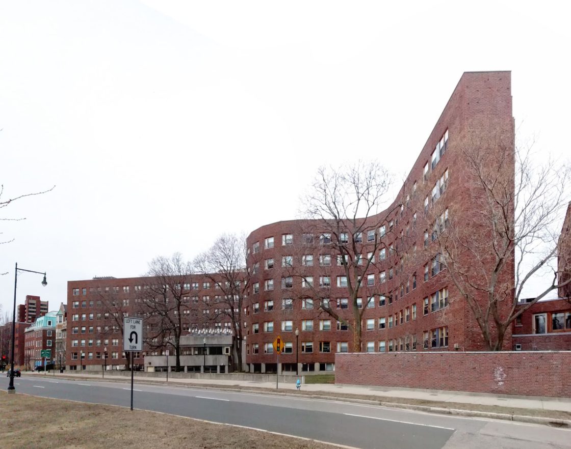 Vista externa da Baker House, residência estudantil projetada por Alvar Aalto para o MIT, com fachada curva em tijolos vermelhos voltada para uma avenida arborizada em Cambridge, nos Estados Unidos