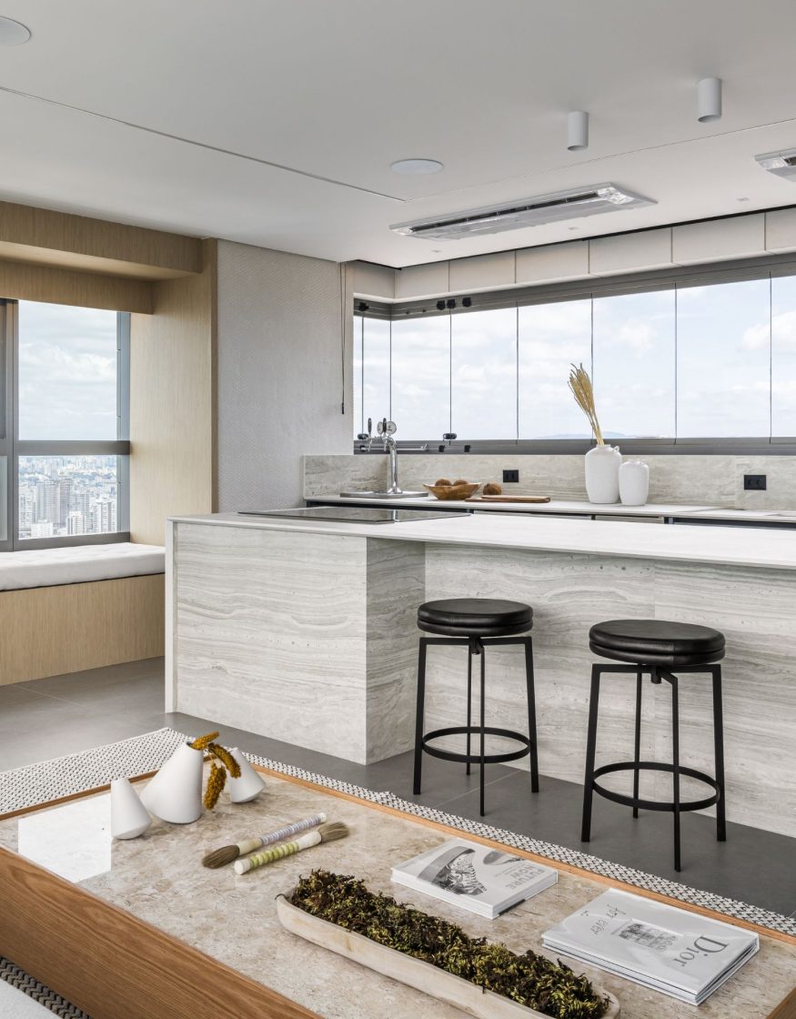 Cozinha clean com bancadas claras, banquetas pretas e uma chopeira em metal prata no canto, próxima à janela