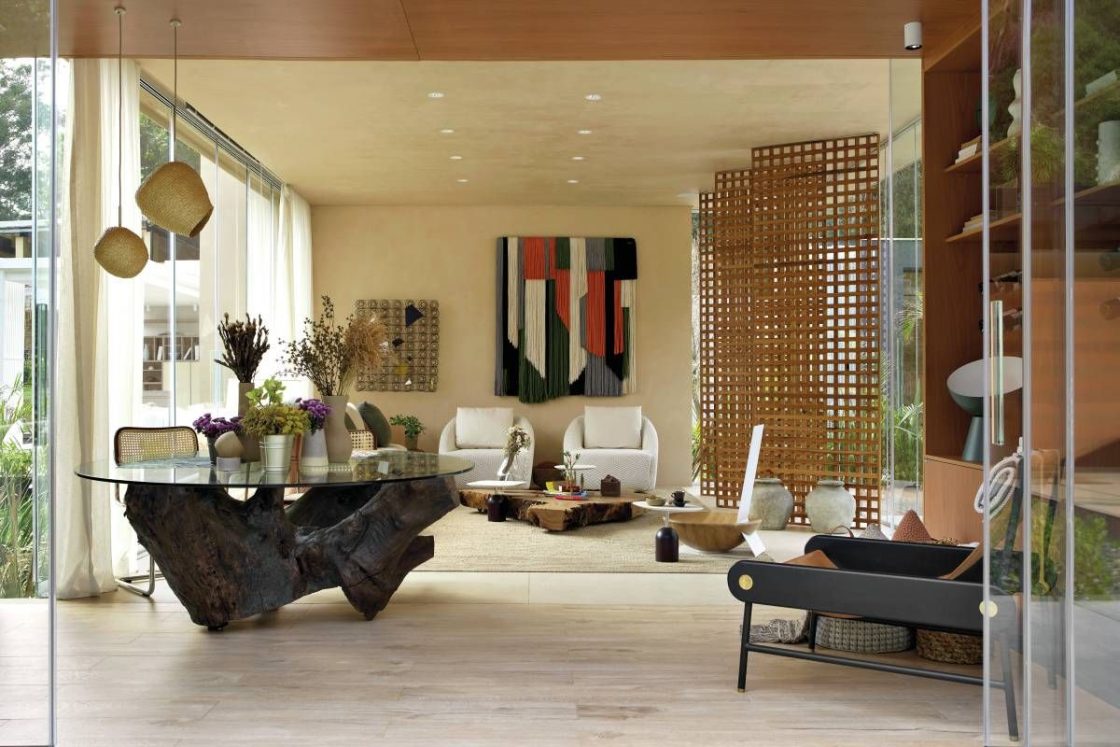 Living amplo e integrado com piso em porcelanato que reproduz madeira, brises de madeira do lado direito e tapeçaria decorando parede ao fundo
