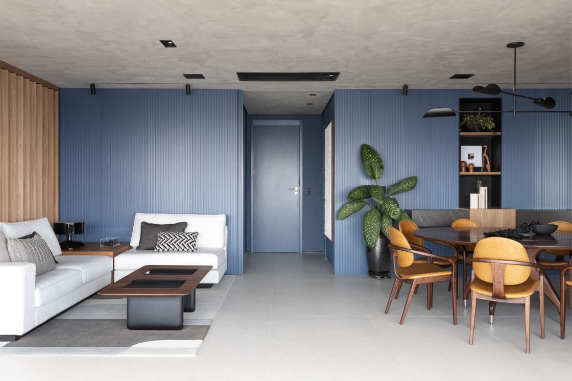 Living integrado à sala de jantar com piso neutro e painel ripado em azul ao fundo