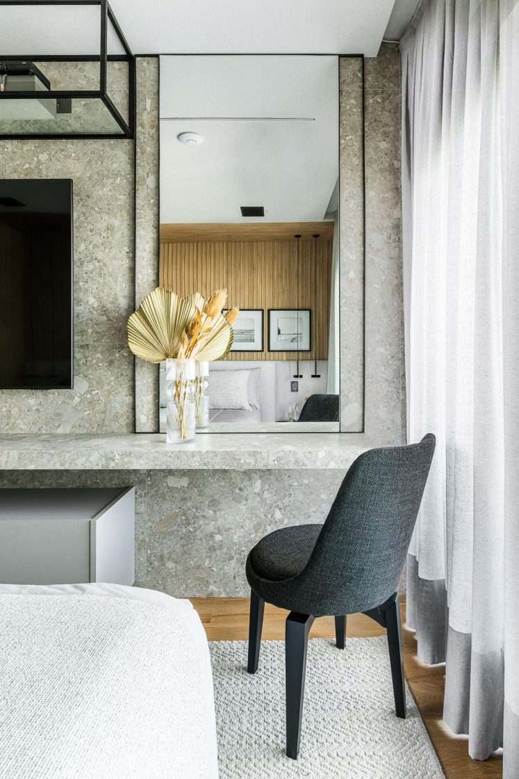 Aparador feito em porcelanato em quarto, com espaço reservado para penteadeira com espelho grande e cadeira em frente