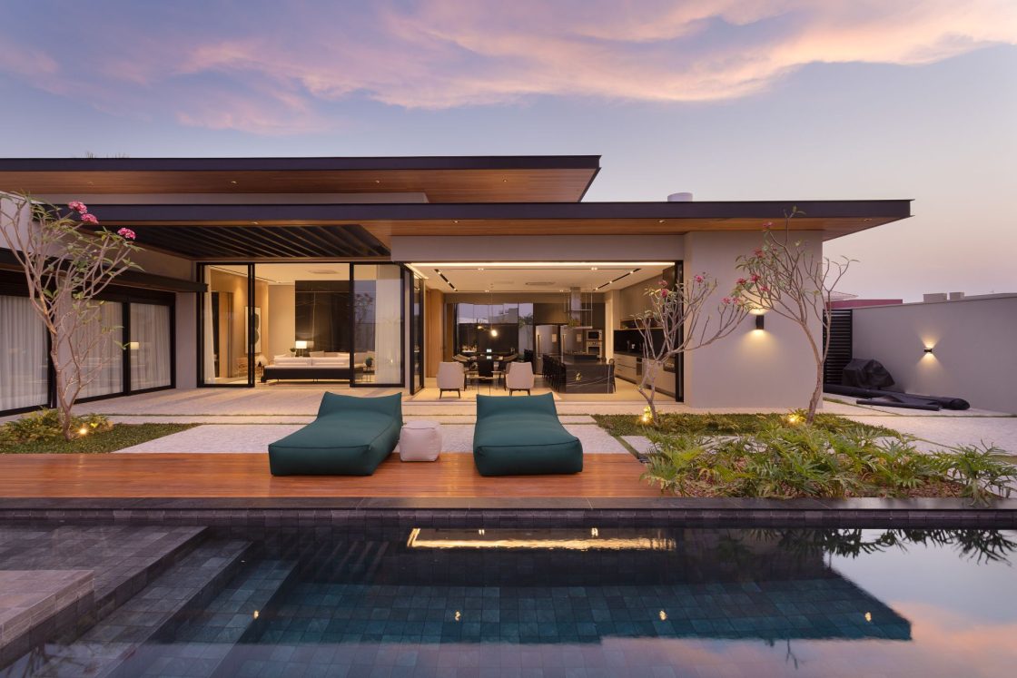 Área externa de casa com piscina de alvenaria e duas espreguiçadeiras no entardecer, com luzes amarelas embutidas acesas