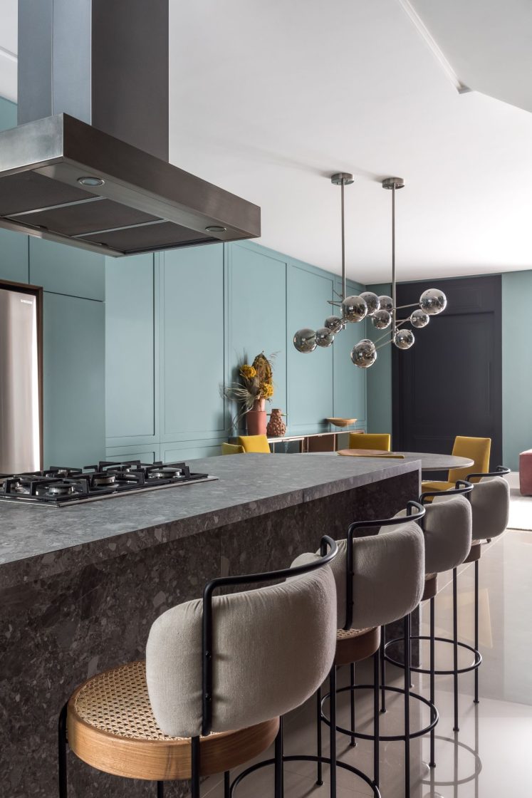 Cozinha com ilha e banquetas em madeira e estofado cinza, com parede ao fundo em verde com boiserie