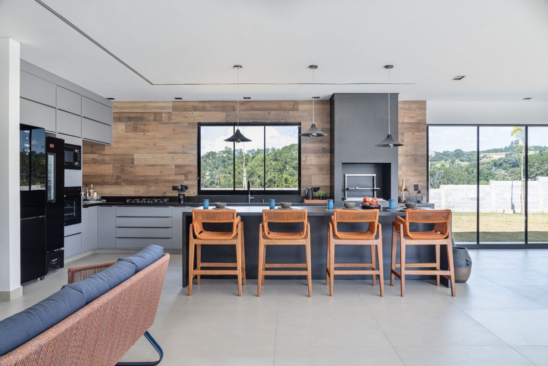 Área gourmet fechada com ilha e decoração rústica, com parede ao fundo em porcelanato que reproduz madeira