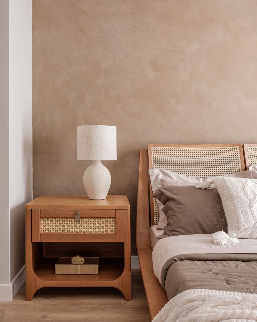Detalhe de cama e mesa de cabeceira em madeira com detalhe de telinha, com piso amadeirado e parede ao fundo em cimento queimado
