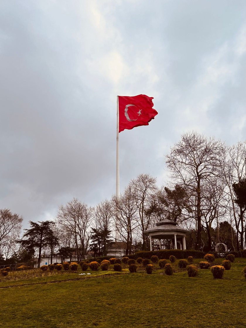 Vista de área verde em Istambul com bandeira turca em destaque, cercada por jardins e árvores sob céu nublado