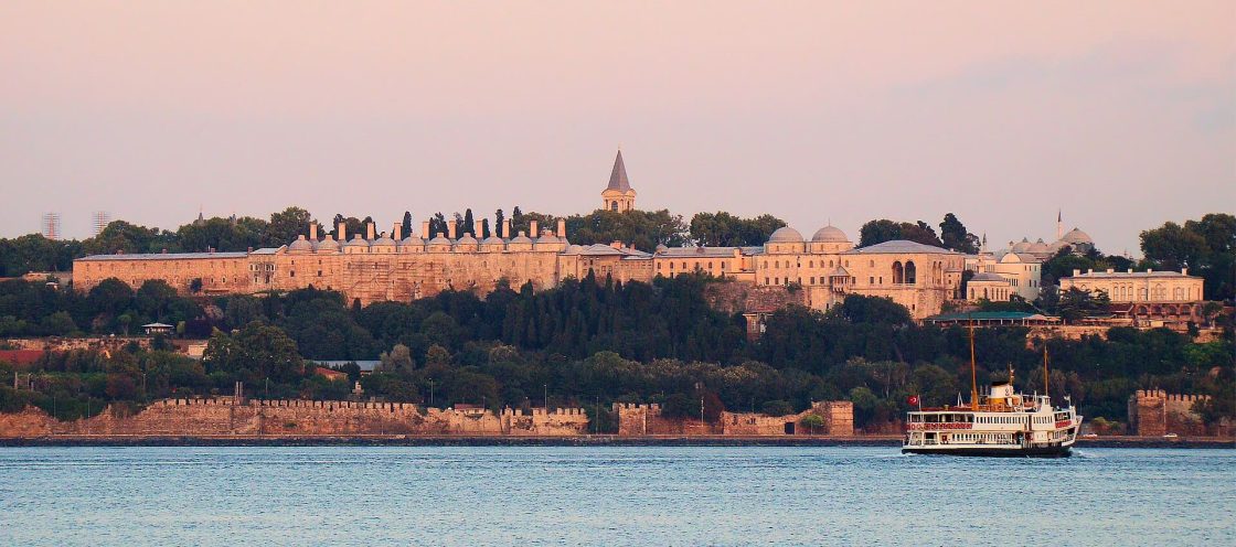 Vista ampla do Palácio de Topkapı, com vegetação, muralhas históricas e águas do Bósforo ao entardecer