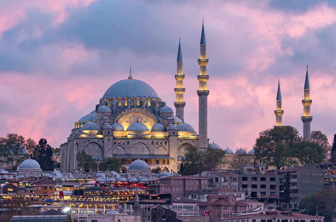 Vista da Mesquita de Süleymaniye iluminada ao entardecer, com sua grande cúpula central e minaretes dominando o horizonte de Istambul