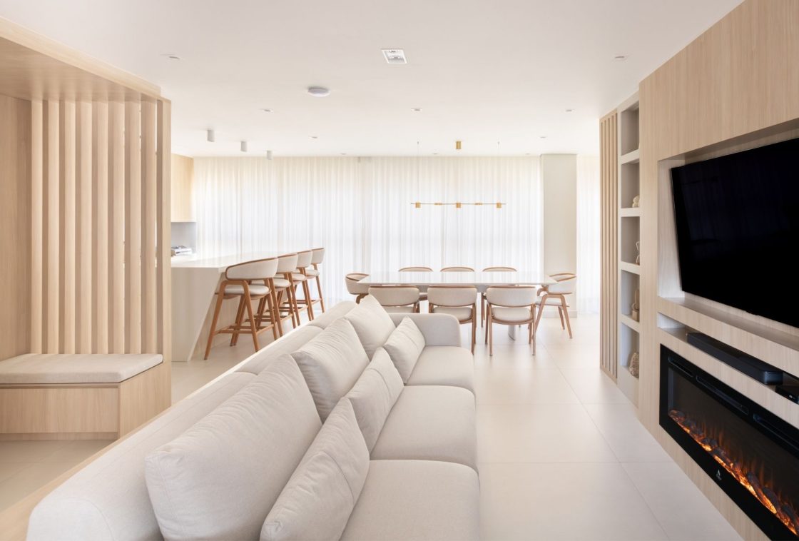 Sala de TV, sala de jantar e cozinha em ambiente integrado no estilo minimalista. No painel principal, há uma lareira elétrica embutida na marcenaria