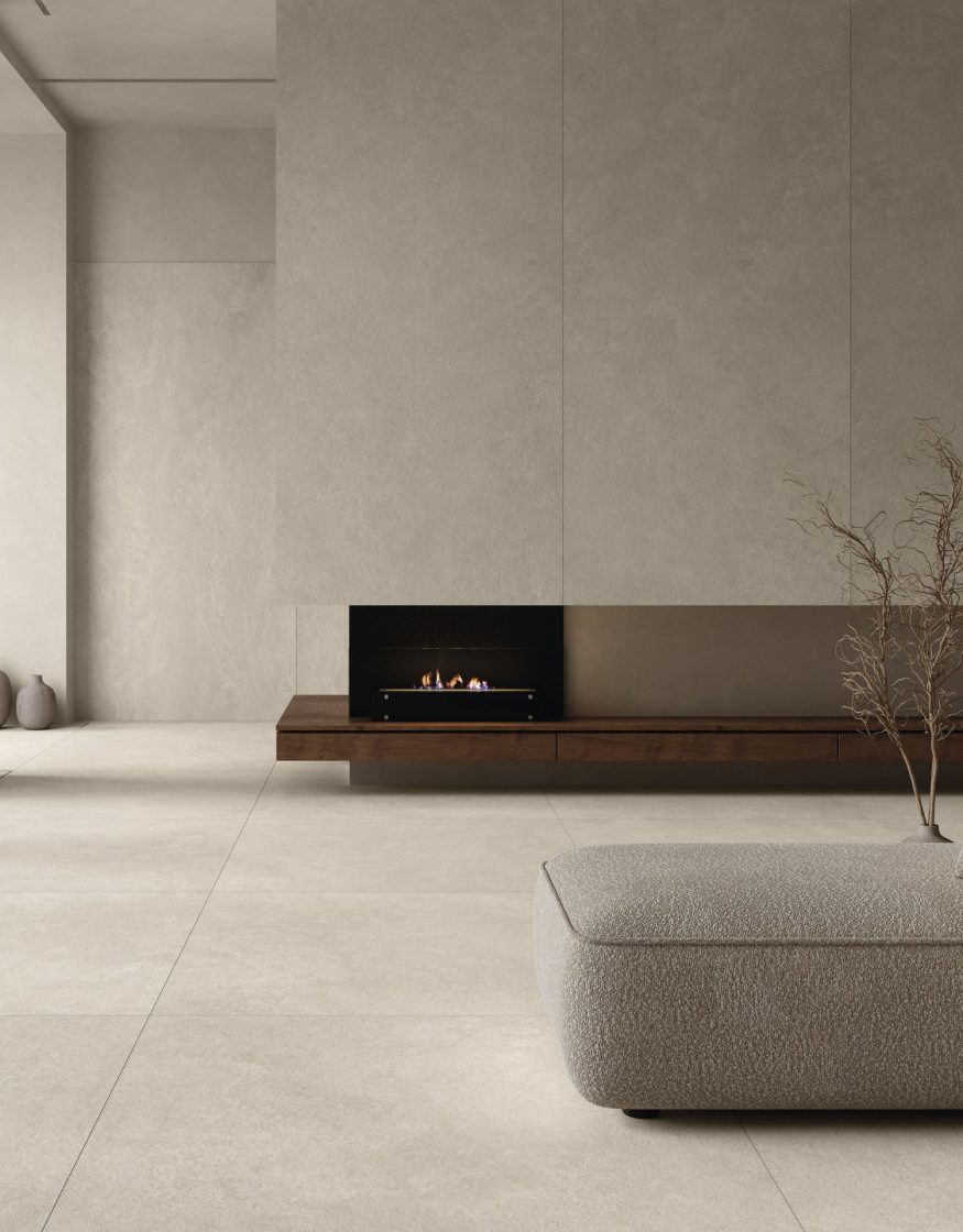 Ambiente contemporâneo com lareira elétrica embutida em parede revestida em porcelanato, com pequenos vasos no piso e um sofá pufe lateral