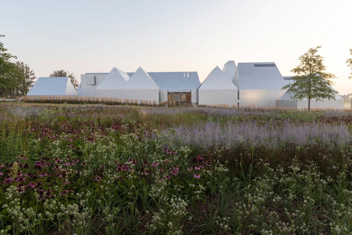 Construção de museu que se parece com casas brancas com telhado colonial, com plantação de flores roxas no entorno